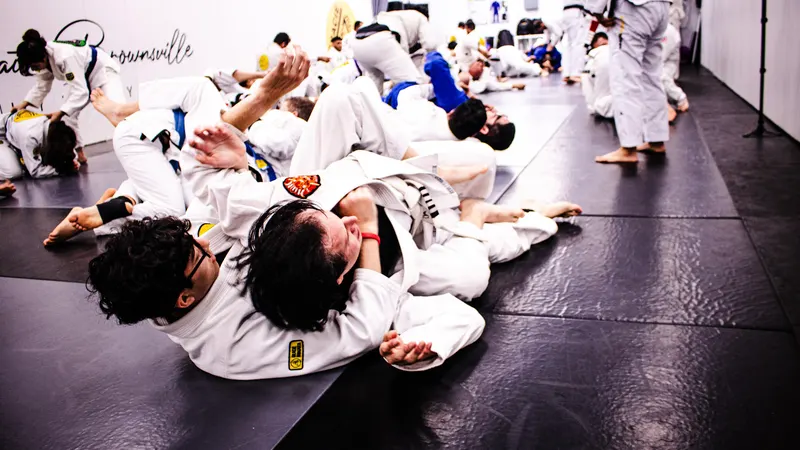 Rows of students in gis practicing a ground technique together on the mat